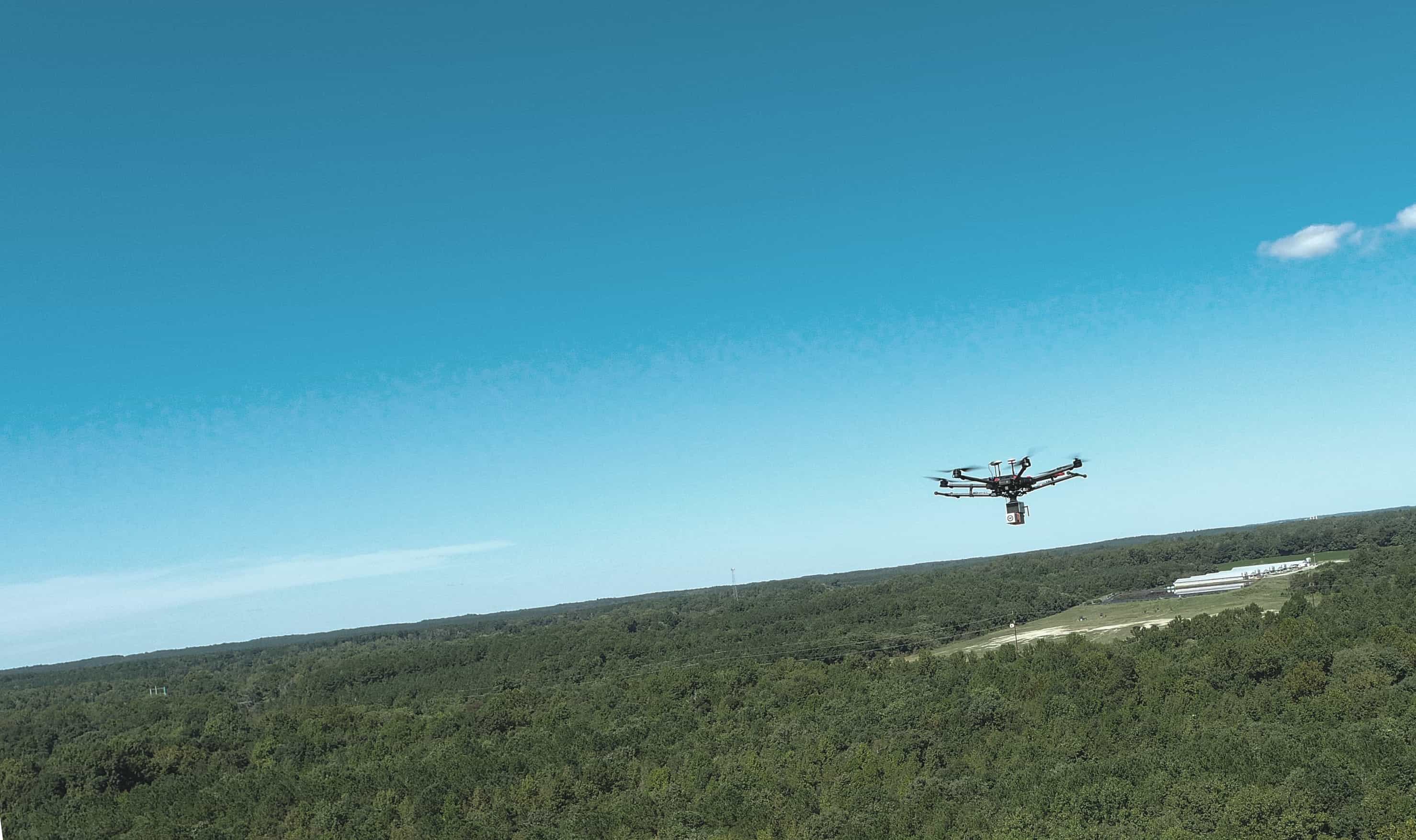 A drone flying above a forest in a clear blue sky